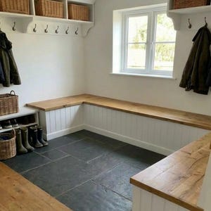 May include: A mudroom with a built-in bench and storage. The bench has a wooden top and white paneling. Wicker baskets sit on shelves above, and hooks are mounted on the wall. The floor is dark gray tile.