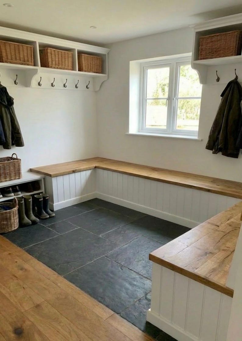 May include: A mudroom with a built-in bench and storage. The bench has a wooden top and white paneling. Wicker baskets sit on shelves above, and hooks are mounted on the wall. The floor is dark gray tile.
