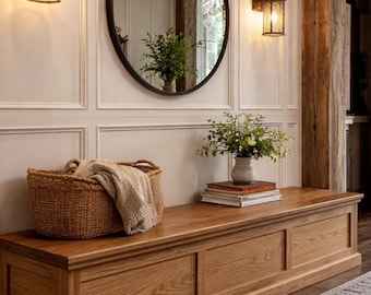 May include: A long rectangular wooden bench with a natural grain finish, featuring a woven basket containing a beige throw blanket, a stack of books, and a small vase with green foliage, positioned beneath a round mirror and two wall sconces.