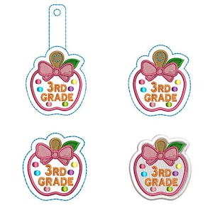 以下が含まれることがあります： ピンクのリボン、緑の葉、オレンジ色の「3RD GRADE」の文字が刺繍された、リンゴ型のワッペン4点。デザインにはカラフルな水玉模様と茶色の茎が含まれています。3つのワッペンには青い点線の輪郭があり、1つにはタブが付いています。