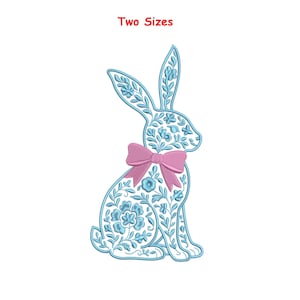 Pode incluir: Um coelho bordado em azul claro com detalhes florais e um laço rosa. A imagem inclui o texto "Two Sizes" em vermelho. O coelho é um item decorativo, possivelmente para a Páscoa ou primavera.