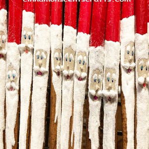 May include: Close-up of several cinnamon sticks decorated with red tips and white, snowy sections. Each stick features a Santa Claus face with blue eyes, a pink mouth, and a white beard. The website address cinnamonscentscrafts.com is visible at the top.