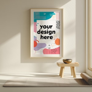 Könnte beinhalten: Ein gerahmtes Poster mit dem Text "your design here" vor einem farbenfrohen abstrakten Hintergrund. Das Poster hängt an einer cremefarbenen Wand. Ein kleiner Holzschemel mit einer Schale und einer Yogamatte befinden sich vor der Wand.