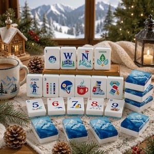 May include: A set of white rectangular mahjong tiles featuring colorful winter-themed illustrations, including mountains, a cabin, a mug, and sports gear. Some tiles display numbers one through nine, while others show the letters W, N, and the word GREEN.