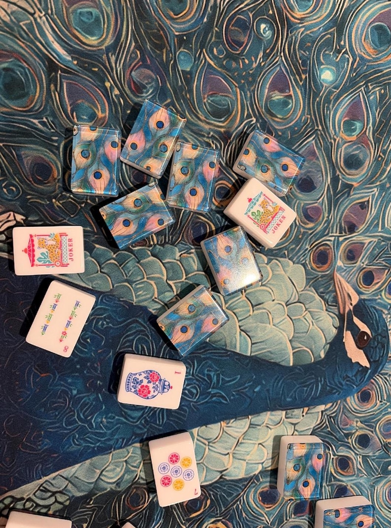May include: A collection of rectangular mahjong tiles featuring various designs, including peacock feather patterns, floral vases, colorful circles, and two tiles labeled JOKER with a giraffe illustration, scattered across a peacock feather print.