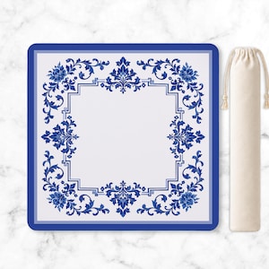 May include: A square mat featuring a white center surrounded by a blue and white floral damask border with intricate scrollwork and a geometric frame. Beside the mat is a beige drawstring fabric pouch with matching light-colored cord ties.