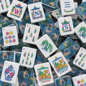 May include: A collection of rectangular mahjong tiles featuring white faces with colorful illustrations of dragons, leopards, floral vases, and directional letters W, N, and S. The backs of the tiles display a detailed blue and green peacock feather pattern.