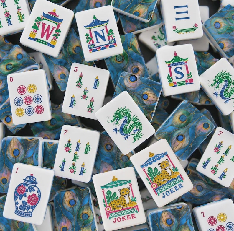 May include: A collection of rectangular mahjong tiles featuring white faces with colorful illustrations of dragons, leopards, floral vases, and directional letters W, N, and S. The backs of the tiles display a detailed blue and green peacock feather pattern.