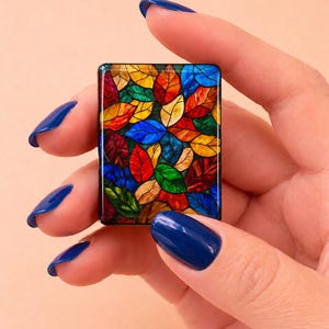 May include: A rectangular tile featuring a vibrant stained glass pattern of overlapping leaves in shades of red, yellow, blue, and green. The design is enclosed within a thin black border, creating a mosaic effect with distinct dark outlines.