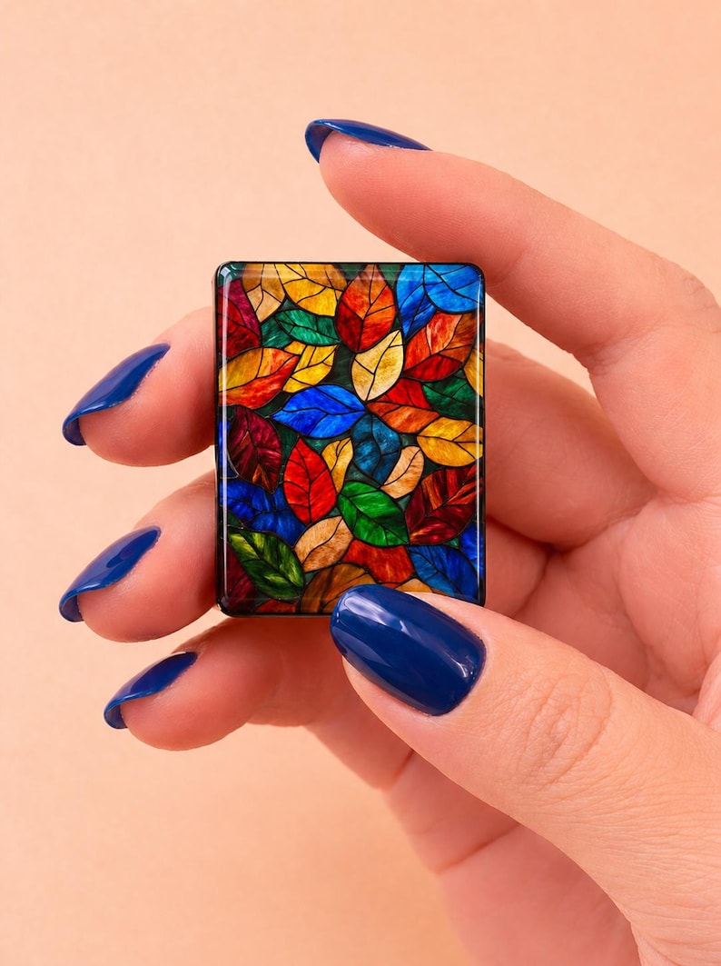 May include: A rectangular tile featuring a vibrant stained glass pattern of overlapping leaves in shades of red, yellow, blue, and green. The design is enclosed within a thin black border, creating a mosaic effect with distinct dark outlines.