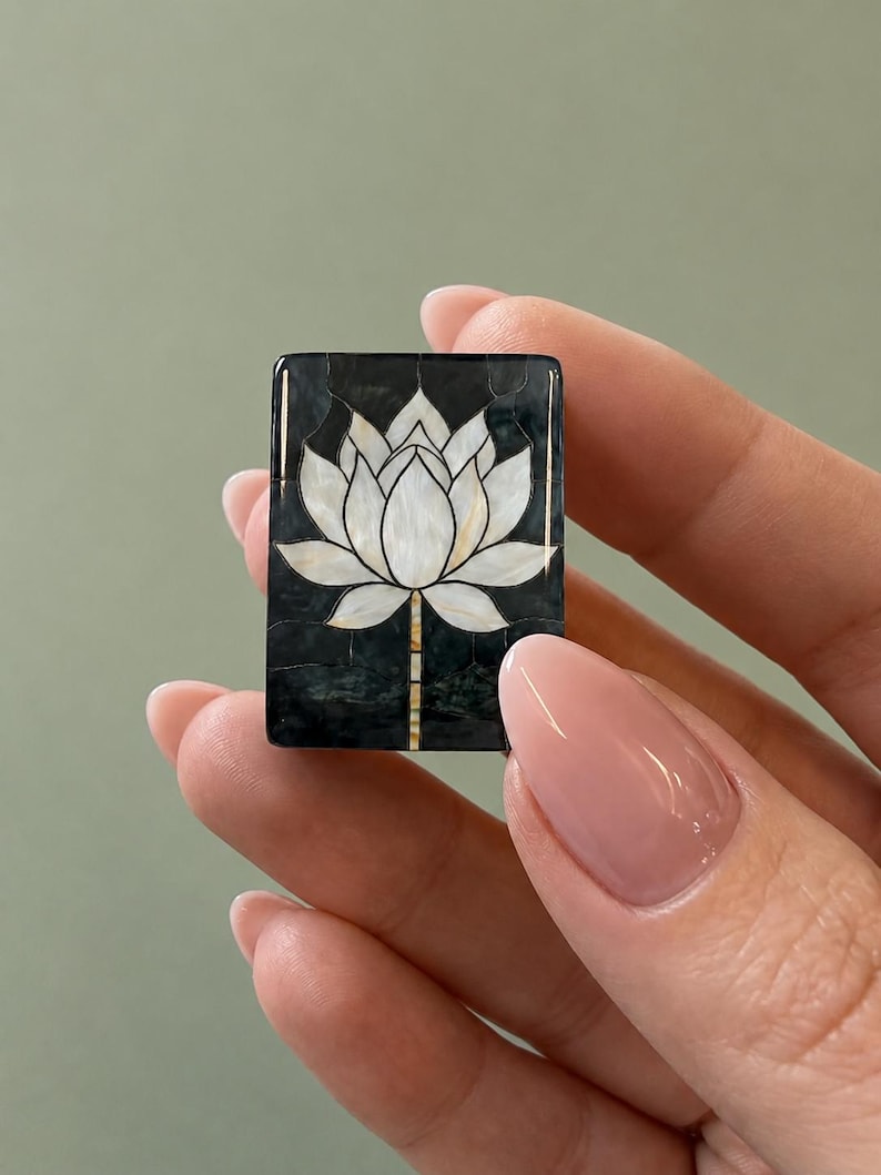 May include: A rectangular inlay piece featuring a white mother-of-pearl lotus flower design set against a dark, mottled black background. The lotus petals are segmented with thin dark lines, and the stem extends downward in a vertical pattern.