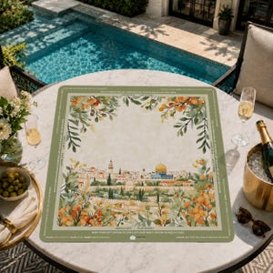 May include: A rectangular placemat with a watercolor illustration of a cityscape, featuring a golden-domed building and surrounding buildings. The placemat has a green border with text and floral accents. The placemat is on a round table with drinks and snacks.