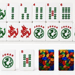 May include: A collection of white rectangular Mahjong tiles featuring green and red dragon illustrations, numbered bamboo suits, and tiles labeled JOKER with a circular dragon emblem. Two tiles display a colorful stained-glass leaf pattern.