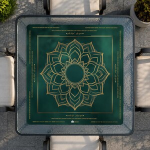 May include: A square glass-topped table with a green and gold game board. The board features a gold floral design in the center and text around the edges. The table is surrounded by four chairs.