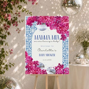 Può includere: Un cartello di benvenuto rettangolare per baby shower su un cavalletto in legno con motivi a piastrelle blu e bianche, vivaci grappoli di fiori rosa e illustrazioni di palle da discoteca. Il testo recita: MAMMA MIA we are having a baby! WELCOME TO Charlotte's BABY SHOWER 30.05.20XX.