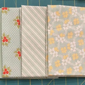 May include: Four fabric squares in a light green color with different patterns. One square has a solid color, one has a white polka dot pattern, one has a white and gray stripe pattern, and one has a yellow and white floral pattern.