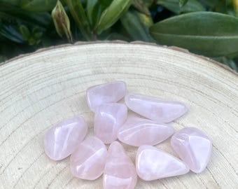May include: A collection of nine tumbled rose quartz stones with a smooth, polished finish and a translucent pale pink color. The stones are irregular in shape, varying in size, and exhibit a soft, glossy luster across their rounded surfaces.