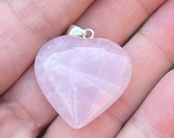 May include: A heart-shaped rose quartz pendant with a smooth, polished surface and a pale pink translucent appearance. The gemstone is attached to a small, silver-toned metal bail at the top, designed for threading onto a necklace chain.