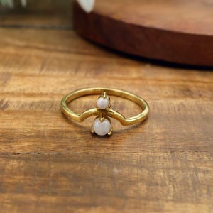 May include: A gold-colored ring with a unique design. The ring features a curved band and two white, round gemstones. The gemstones are set in a decorative setting, adding a touch of elegance to the jewelry.