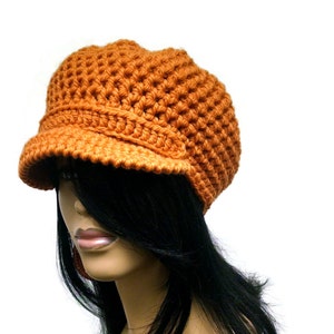 Puede incluir: Un gorro de punto naranja con visera. El gorro está hecho con un punto texturizado.