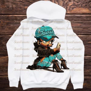 May include: White hoodie featuring a cartoon character wearing a teal cap with "Taurus" text. The character is holding a phone, dressed in teal patterned pants and black jacket, and high-heeled boots. The design has a cartoonish style.