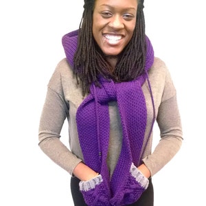 May include: A purple knitted infinity scarf with pockets on the ends. The scarf is worn by a person with long black dreadlocks.