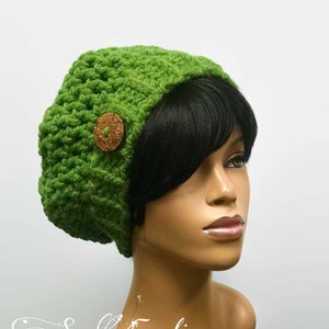 Puede incluir: Un gorro de punto verde con un botón marrón. El gorro es holgado y tiene un ala ancha.