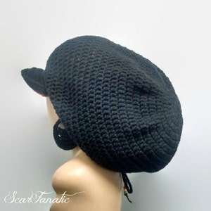 Puede incluir: Un sombrero negro de ganchillo con una pequeña visera y un cordón. El sombrero está hecho de hilo texturizado y tiene forma redonda. El sombrero se muestra en una cabeza de maniquí.