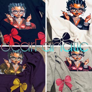 Könnte beinhalten: Vier Sweatshirts in verschiedenen Farben mit einem Cartoon-Bild einer Frau mit einer roten Schleife auf der Vorderseite. Die Frau trägt eine schwarze Jacke, eine goldene Halskette und Ohrringe. Die Sweatshirts sind schwarz, weiß, lila und grau.