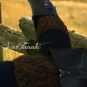May include: Brown knitted leg warmers with a black boot. The boot has a zipper and a buckle. The leg warmers are a cable knit pattern.