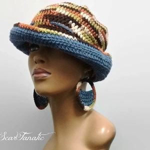May include: A blue and brown crocheted hat with a wide brim. The hat is being worn by a mannequin with large crocheted hoop earrings.