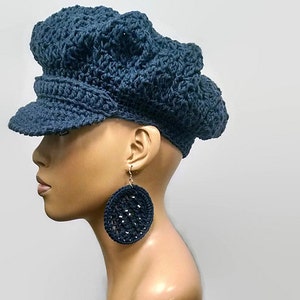 May include: A dark blue crocheted newsboy cap with a wide brim. The cap is worn on a mannequin with large, round, dark blue crocheted earrings.