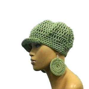 Op de afbeelding: Een groene gehaakte hoed met een brede rand en bijpassende gehaakte oorbellen. De hoed wordt gedragen op het hoofd van een mannequin.