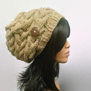 Puede incluir: Un gorro de punto marrón de gran tamaño y ajuste holgado con un botón de cáscara de coco marrón. El gorro lo lleva una persona con el pelo largo y negro.