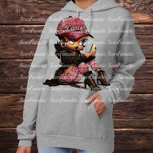 以下が含まれることがあります： 「Cancer」の文字が入ったピンク色の帽子と、お揃いのパンツを履いた漫画のキャラクターが描かれたグレーのパーカー。キャラクターは携帯電話を持っており、黒いハイヒールブーツを履いています。