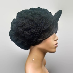 Puede incluir: Un gorro negro de punto con una corona grande y redonda y un borde pequeño. El gorro tiene un patrón de punto de cable y un diseño único y doblado.