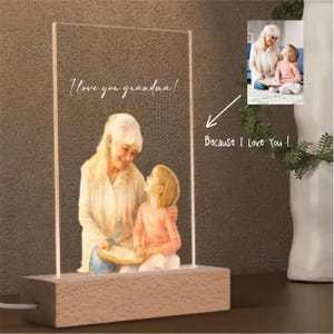 May include: A lighted acrylic panel with an illustration of a grandmother and granddaughter, with the text "I love you grandma!" and "Because I Love You!". The base is a rectangular wooden block.