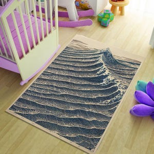 Könnte beinhalten: Rechteckiger Teppich mit einem stilisierten Ozeanwellen-Design in Blau- und Beigetönen. Der Teppich liegt auf einem hellen Holzboden, mit einem Kinderbett und Spielzeug im Hintergrund. Das Design des Teppichs erinnert an das Meer. Ca. 150 cm x 200 cm.