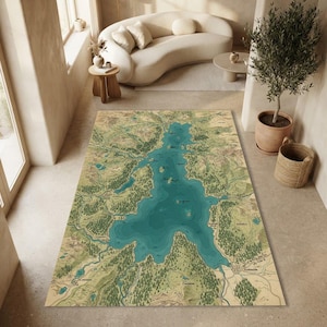 Könnte beinhalten: Ein rechteckiger Teppich mit einer detaillierten topografischen Karte eines Sees und der umliegenden Landschaft. Das Design zeigt tiefblaugrünes Wasser im Kontrast zu gedämpftem Grün und Beige, ergänzt durch Ortsnamen und Waldsymbole.