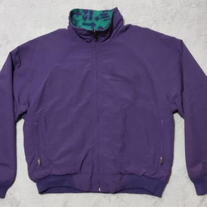 Puede incluir: Chaqueta morada con cremallera completa, dos bolsillos laterales y cuello con estampado verde y azul. La chaqueta tiene puños y dobladillo elásticos. Fabricada con un material ligero.
