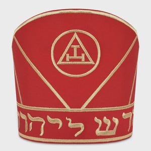 May include: A red ceremonial hat with gold embroidered accents. The hat features a gold embroidered emblem within a circle and Hebrew text at the base. Gold lines accent the hat's design.