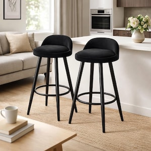 May include: Two black bar stools with rounded seats and backs. The stools have black metal legs and footrests. The stools are in a kitchen setting with a neutral colour scheme.