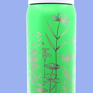 Pu&ograve; includere: Una borraccia verde con un design floreale. La bottiglia ha un coperchio viola chiaro e un bordo bianco. Il design floreale &egrave; argentato e presenta vari fiori e foglie. La parola "wala" &egrave; stampata sulla bottiglia.