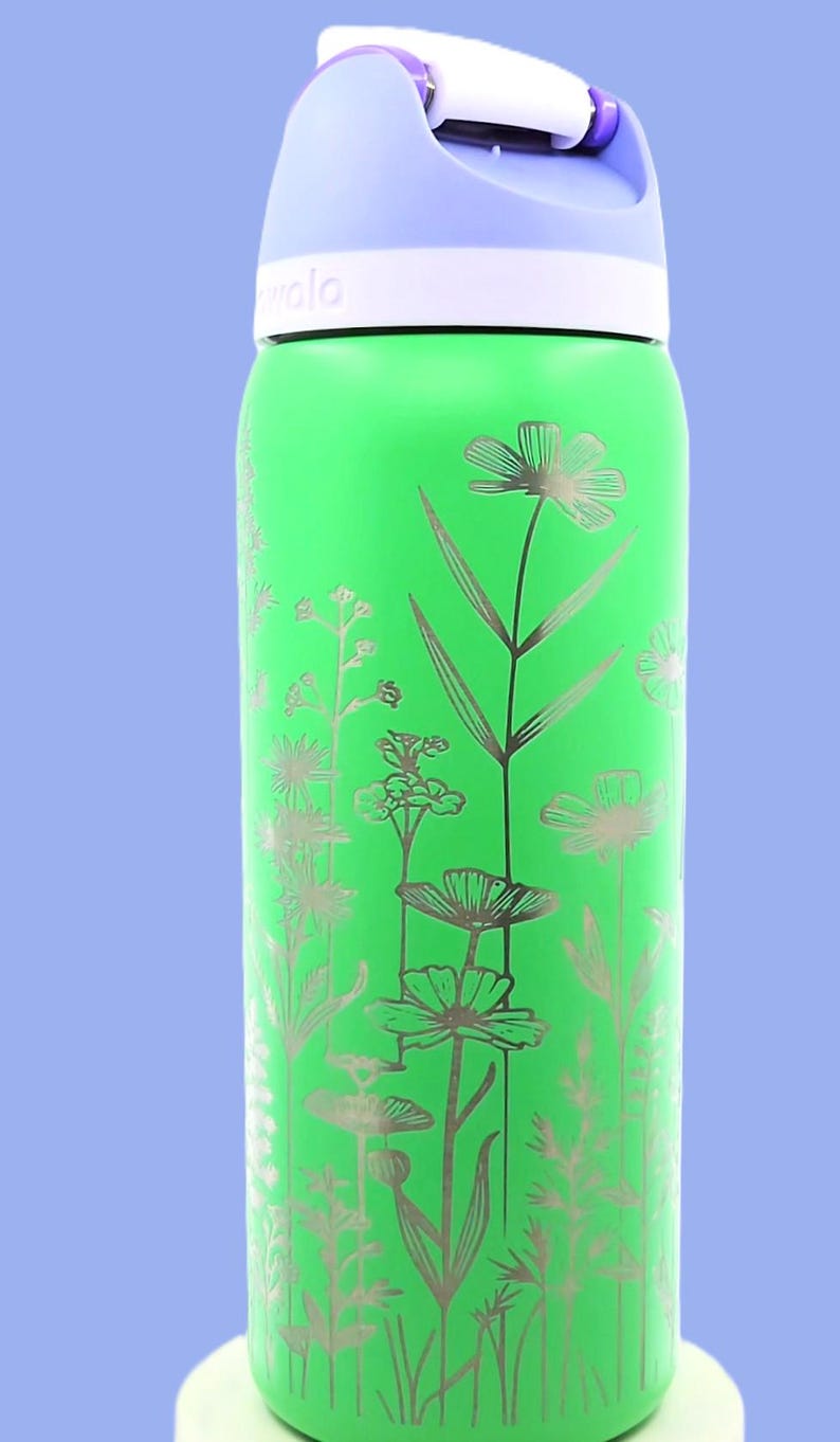 Pu&ograve; includere: Una borraccia verde con un design floreale. La bottiglia ha un coperchio viola chiaro e un bordo bianco. Il design floreale &egrave; argentato e presenta vari fiori e foglie. La parola "wala" &egrave; stampata sulla bottiglia.