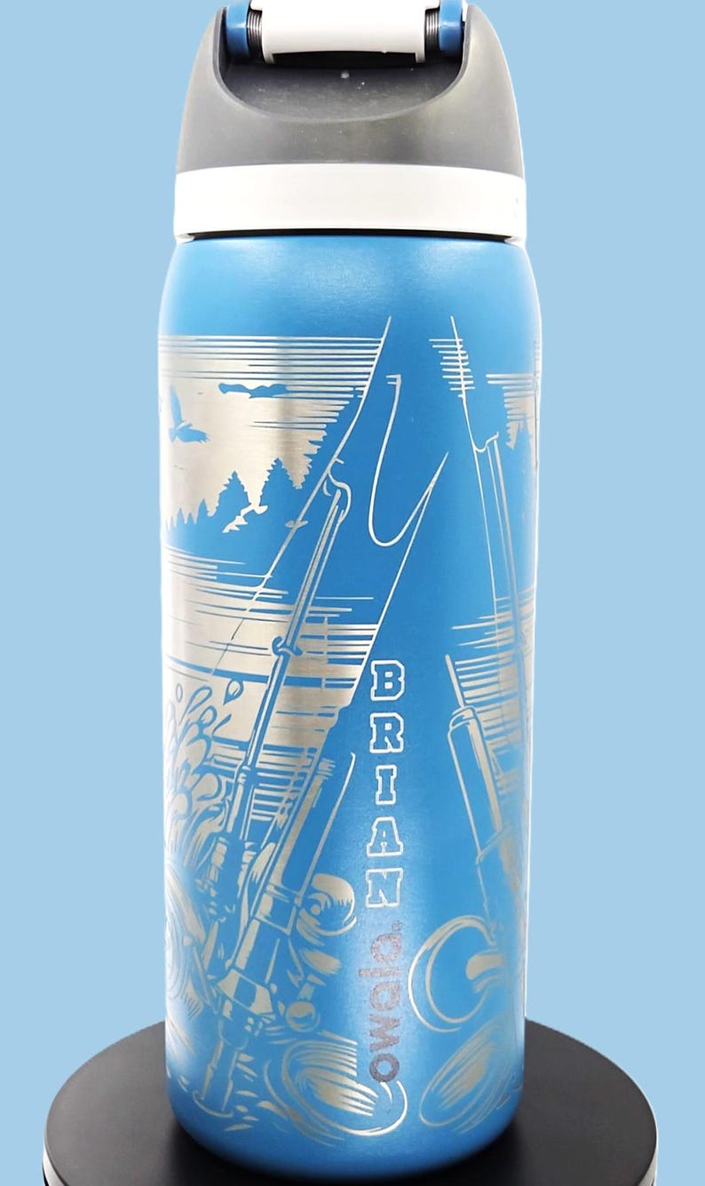 May include: Blue insulated water bottle with a silver fishing scene design. The bottle features the name "BRIAN" vertically and the brand name "Cowala". The lid is gray and white.