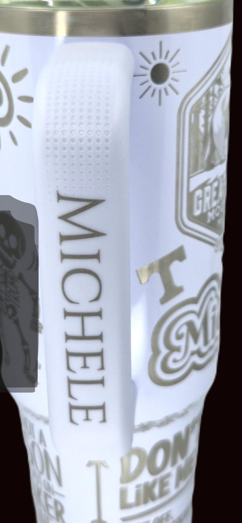May include: White travel mug with a gold rim and handle. The mug features the name "MICHELE" in gold lettering, along with various gold-colored graphics and text, including "Great Smoky Mountains" and "I Love Michele".