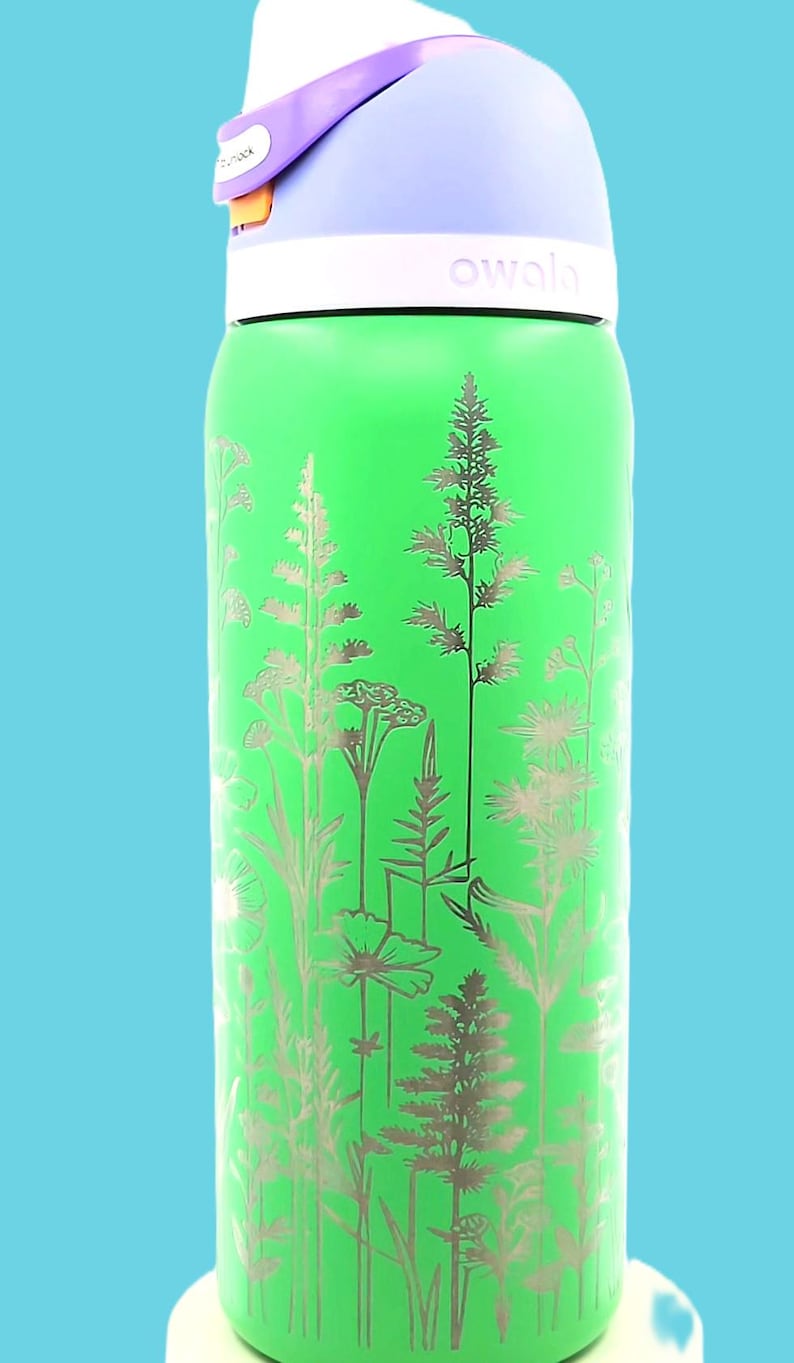 Pu&ograve; includere: Una borraccia verde con un design floreale. La bottiglia ha una parte superiore bianca, un coperchio viola chiaro e il marchio "owala" stampato sul lato. Il design floreale &egrave; argentato e presenta varie piante.