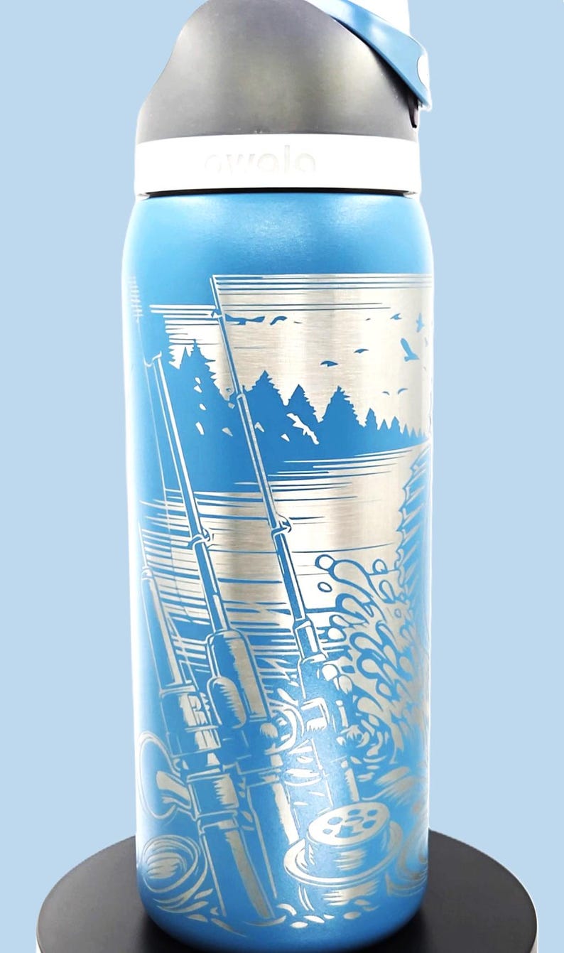 May include: Blue insulated water bottle with a fishing-themed design. The bottle features a detailed illustration of fishing rods, water, trees, and birds. The bottle has a white lid and the brand name "awala" is visible.