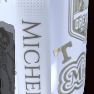 Puede incluir: Una taza de cer&aacute;mica blanca con asa negra y el texto "But First, Coffee" en negrita negra. La taza se encuentra sobre un fondo borroso, sugiriendo un ambiente acogedor.