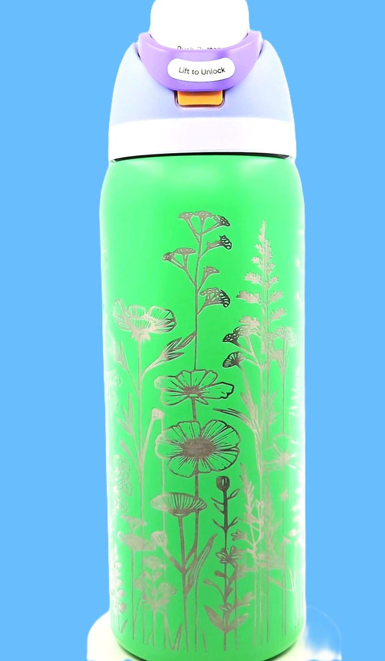 Pu&ograve; includere: Una borraccia verde con un design floreale argentato. Il tappo &egrave; viola e riporta la scritta "Lift to Unlock". Il design floreale presenta vari fiori e piante.